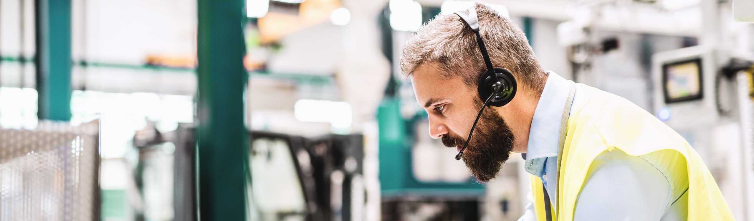 Engineer with a headset is working in a large industrial hall